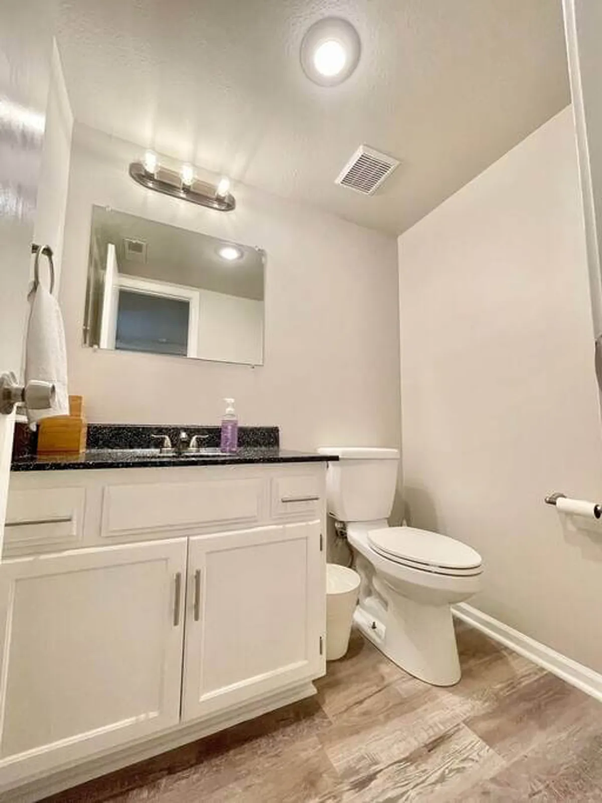 A fresh and inviting full bathroom showcasing a well-lit vanity with sink, a large mirror, toilet, and stylish light fixture. The space is ideal for morning grooming routines or evening wind-downs.