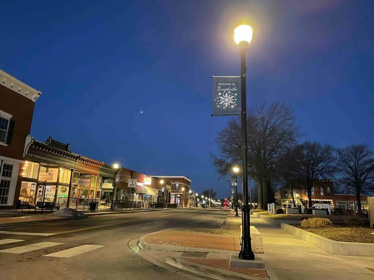 An inviting street view showing shopfronts decorated with banners and illuminated by nostalgic street lamps. The festive details suggest a lively atmosphere, ideal for holiday markets, art fairs, or evening strolls.