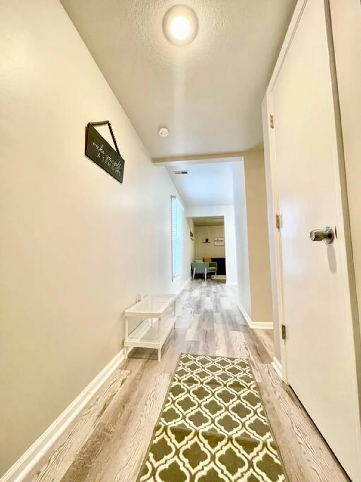 This image depicts the entryway and hallway, featuring a decorative sign, a soft rug, and a small sitting area. It exudes a sense of arrival and a warm transition from the entrance into the heart of the home, setting a welcoming tone for guests.