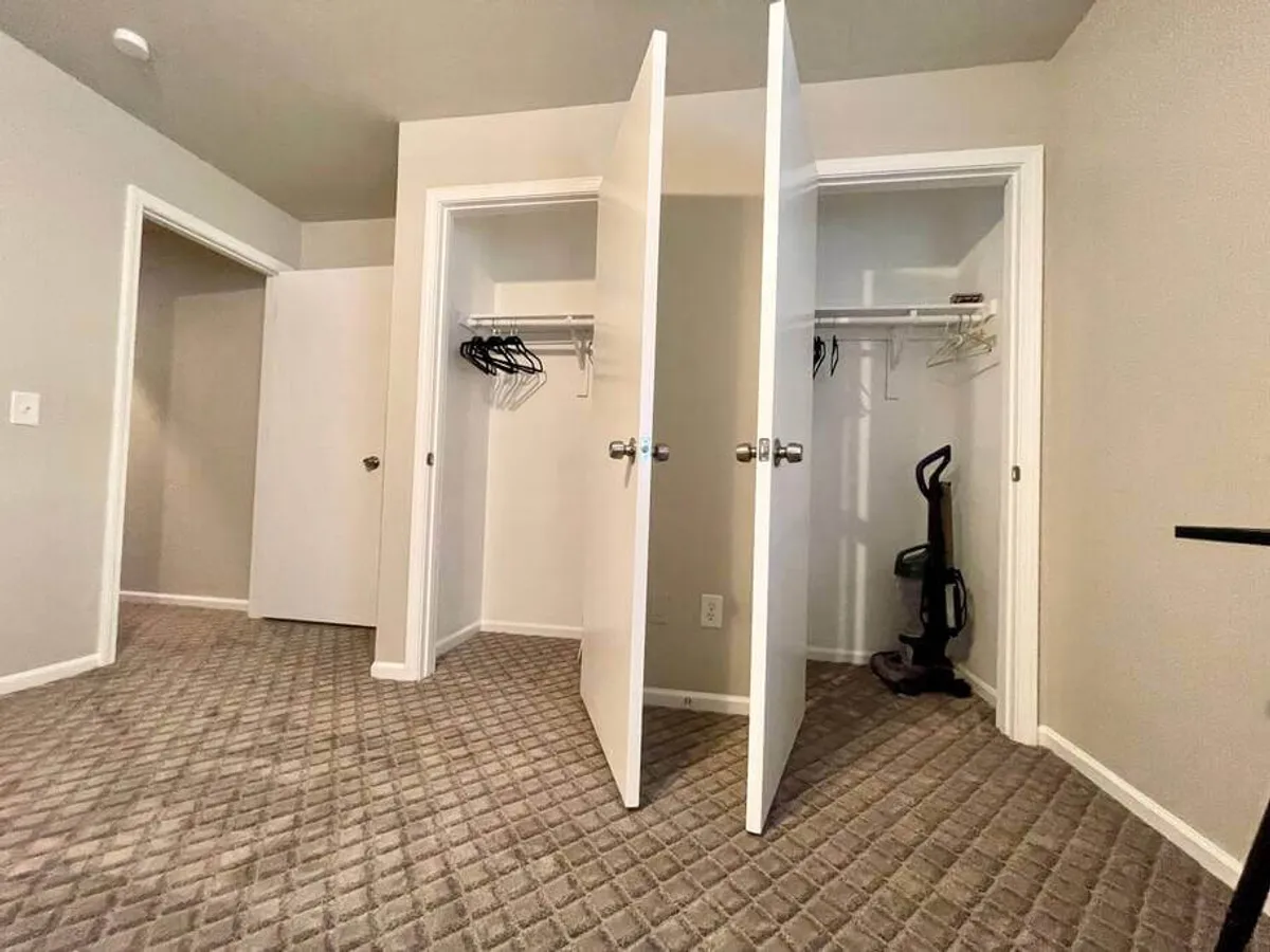 Two open closet doors reveal neatly hanging clothes, ample storage space, and a vacuum cleaner. The area feels functional and thoughtfully arranged, emphasizing everyday practicality and cleanliness.