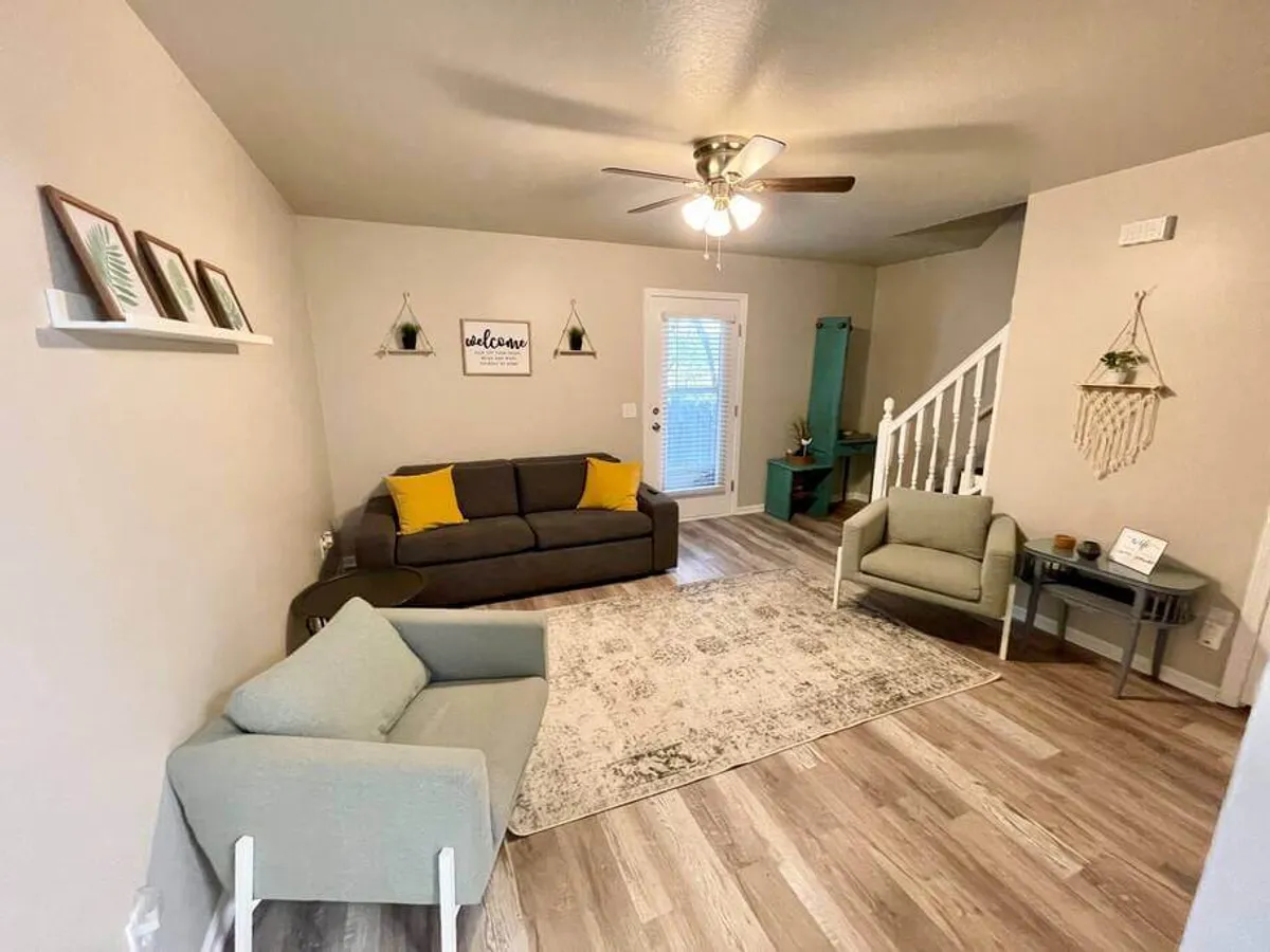 A warm, inviting living room with a plush sofa, coordinating rug, tasteful wall art, and a view through the doorway that hints at the rest of the home. The space is styled for comfort and socializing, featuring soft lighting and cozy seating arrangements.