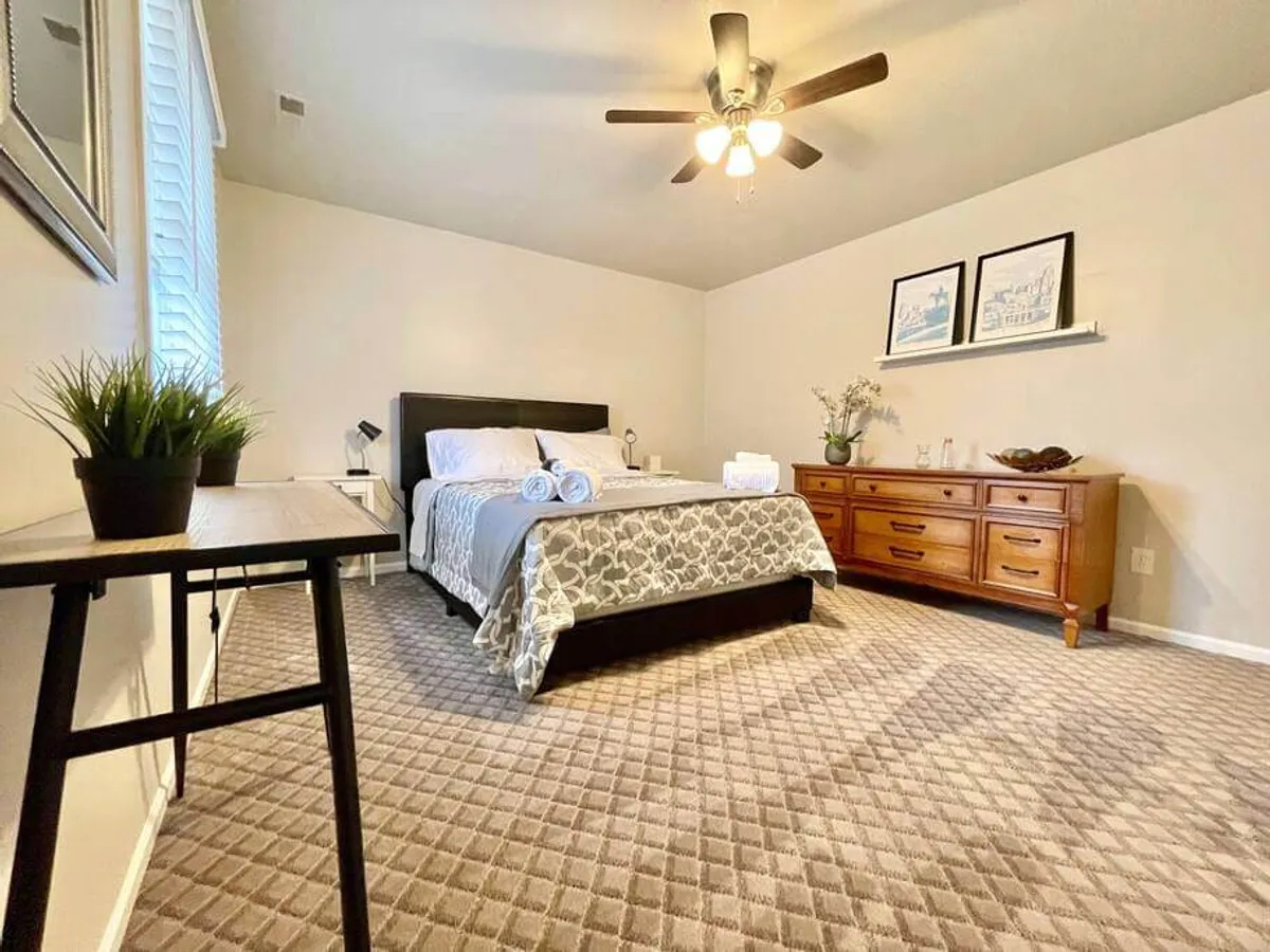 A peaceful bedroom featuring a comfortable bed with decorative bedding, a wooden dresser, tasteful wall art, and a table with a plant. The space feels restful, perfect for enjoying a book or a quiet moment, and offers ample storage via the dresser.
